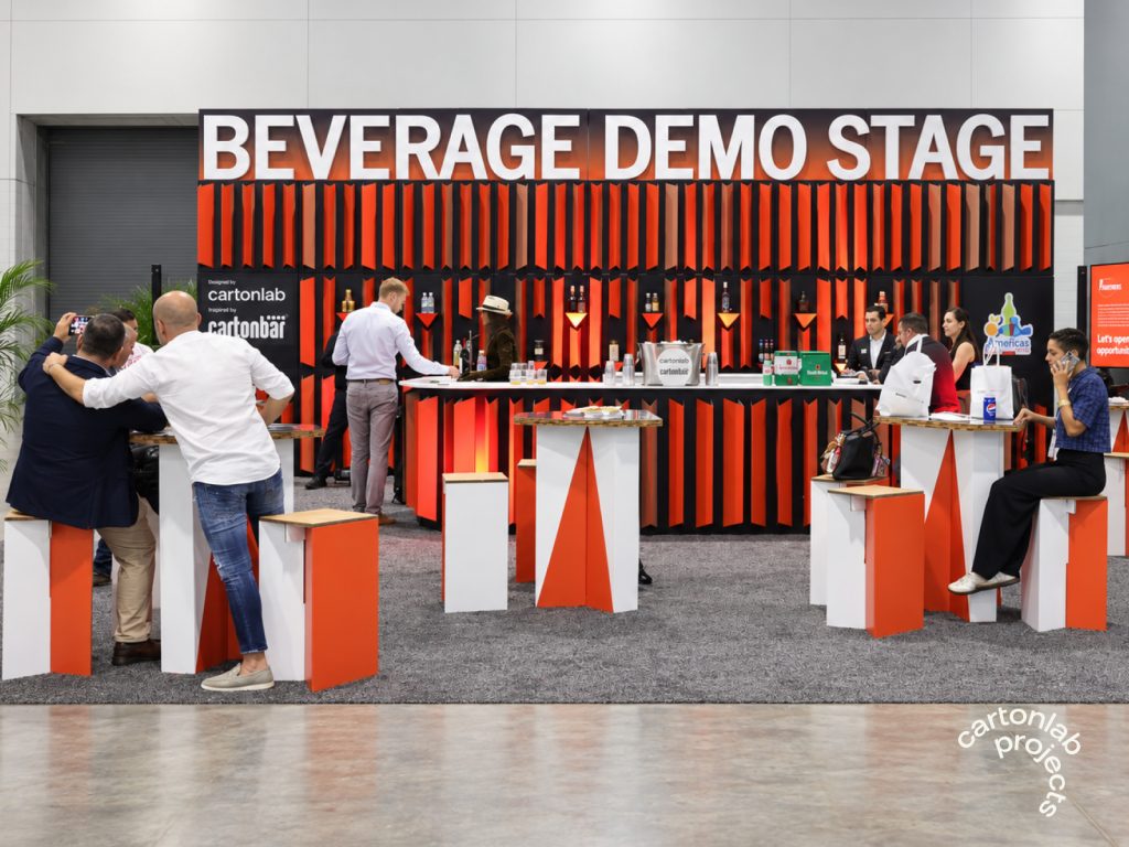 Asistentes junto a la barra del Beverage demo station y mesas altas con taburetes naranjas y blancos