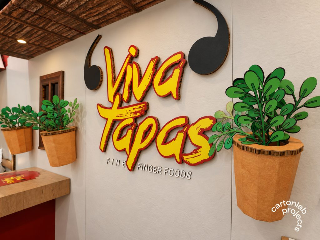 Logotipo de Viva Tapas en la pared del stand, junto a una ventana de madera y macetas con plantas